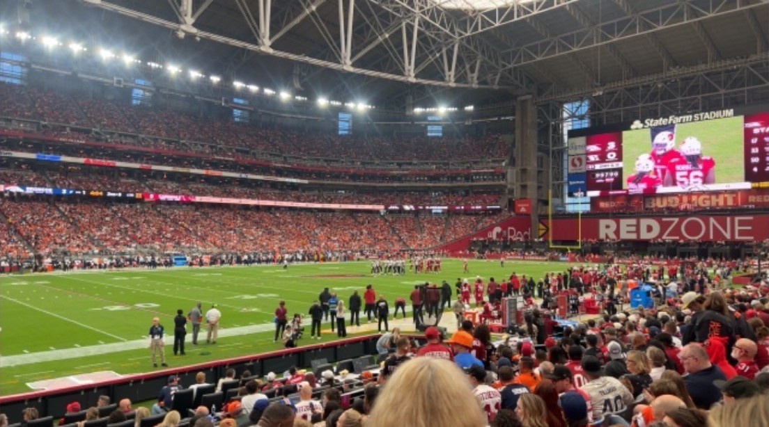State Farm Stadium from the stands at the Broncos–Cardinals game: the field under the roof lights, the RedZone board, Broncos orange across the far stands